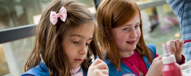 Two Girl Scouts in blue vests decorate clear glass ornaments with paint
