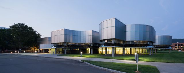Exterior of a metal wavy building with a teal glass stripe at dusk (Photo: Iwan Baan)
