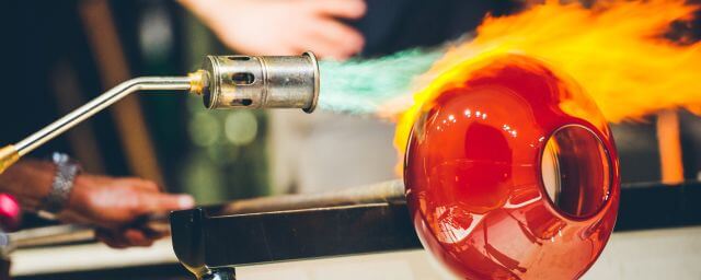 Close-up of a glassblower using flame to heat a red sphere