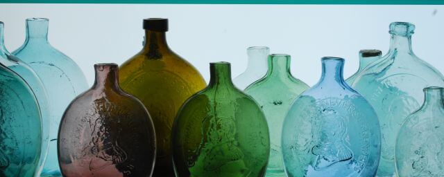 A row of colorful glass flasks on a clear glass shelf