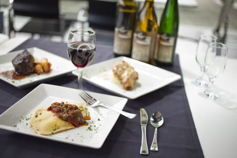 White plates with catered meal options: ravioli, chicken or steak with a variety of wines