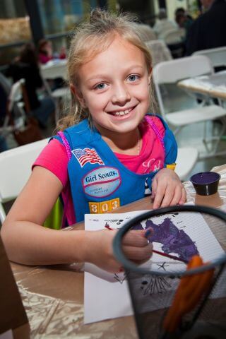 Young Girl Scout in blue vest colors with a purple marker